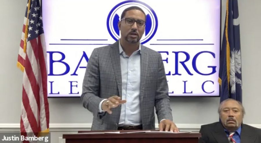 n this screen grab from video provided by Bamberg Law, LLC, attorney Justin Bamberg, standing, speaks at a news conference as plaintiff Jethro DeVane, seated at right, listens, Tuesday, Dec. 22, 2020, in Orangeburg, S.C. DeVane was embarrassed and feared for his life during a June 2019 episode when a Rock Hill police officer looking for teens who might have been breaking into cars held him outside naked and at gunpoint after he peeked out his door to check on the disturbance. (Courtesy of Bamberg Law, LLC via AP)