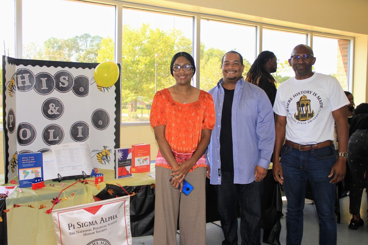 Members of the history and political science faculty, Alicia Hoffman, Ph.D., Maurice Robinson, Ph.D., and Balla Keita, Ph.D. are standing by a Pi Sigma Alpha (National Political Science Honor Society) display during Connection Day in the Dunn-Oliver Acadome